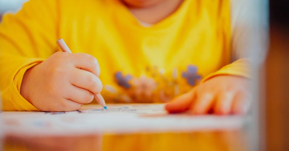 photo of a child in a yellow top drawing on paper