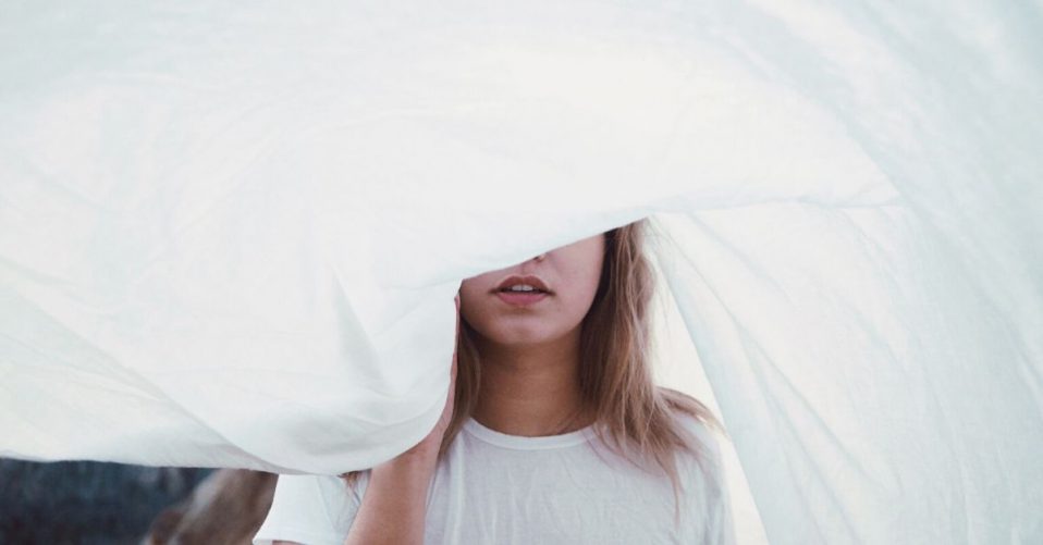photo of a woman in white shirt with her face half shrouded by a big piece of cloth