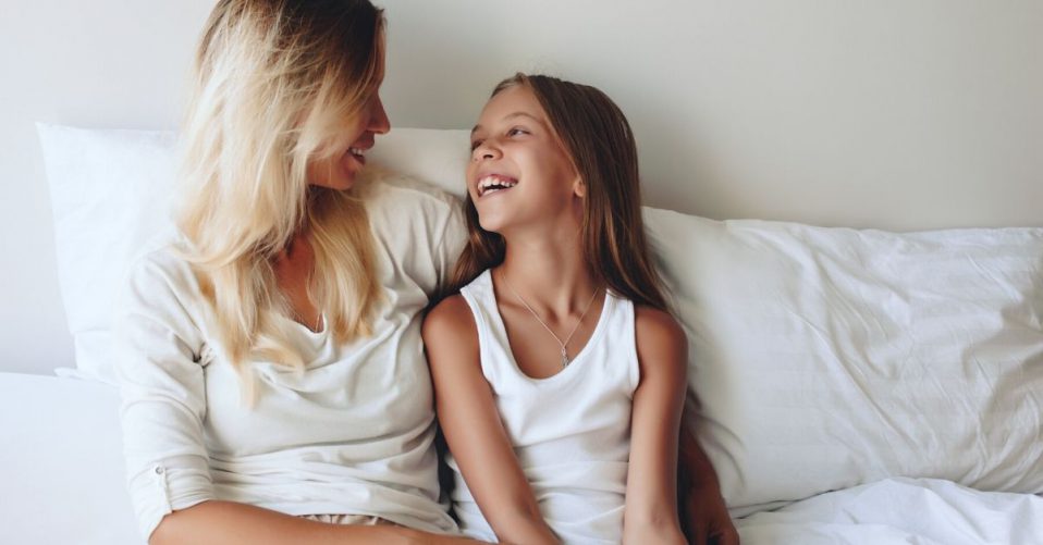 photo of a mother and daighter sitting up against pillows at home laughing and talking