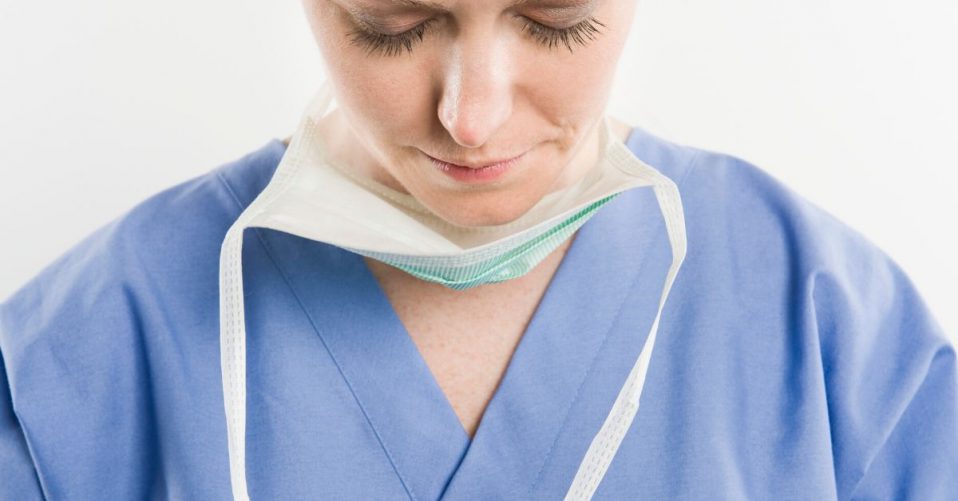 photo of a nurse with fask mask undone and with her head bowed and eyes closed.