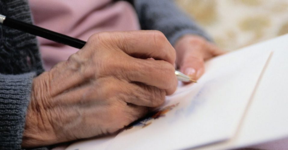 photo depicts close up photo of a hand writing a letter