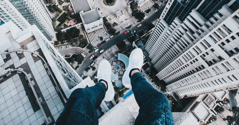 man's feet hanging off the edge of a tall building